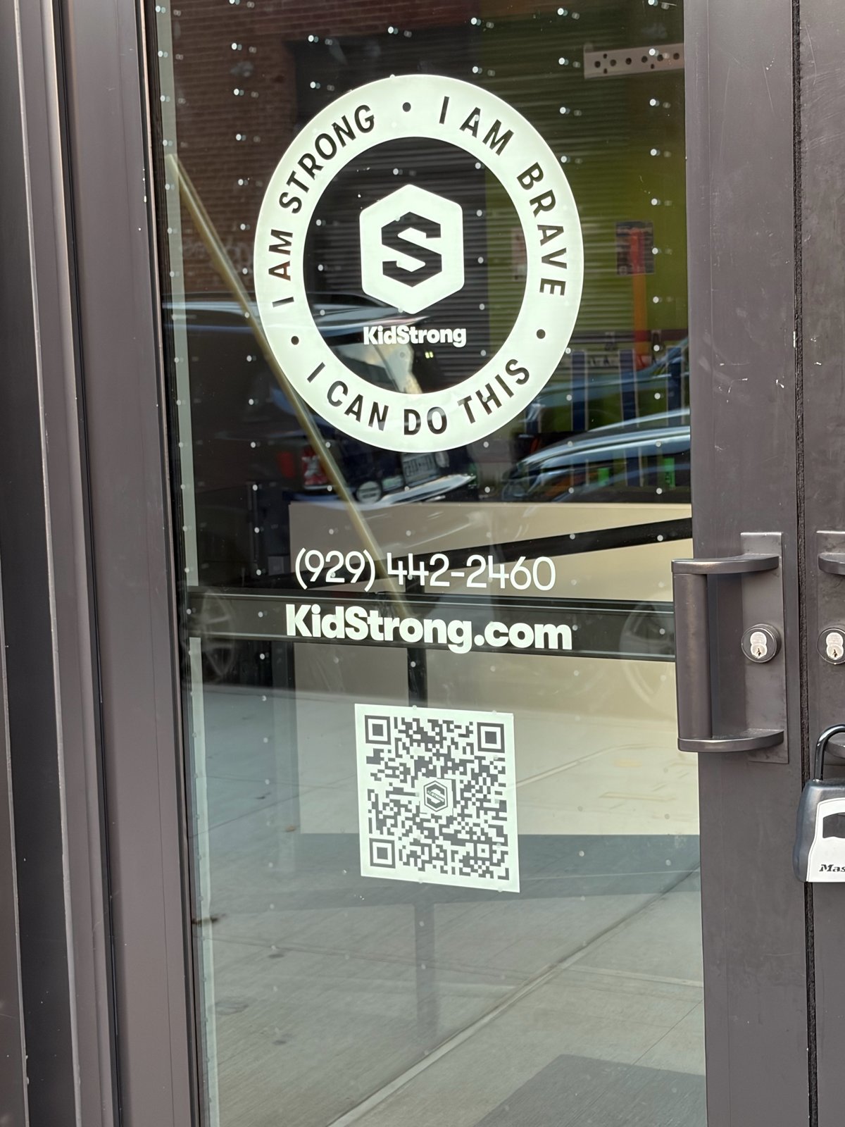 Glass door with a round KidStrong logo decal, a phone number, the website KidStrong.com and a QR code