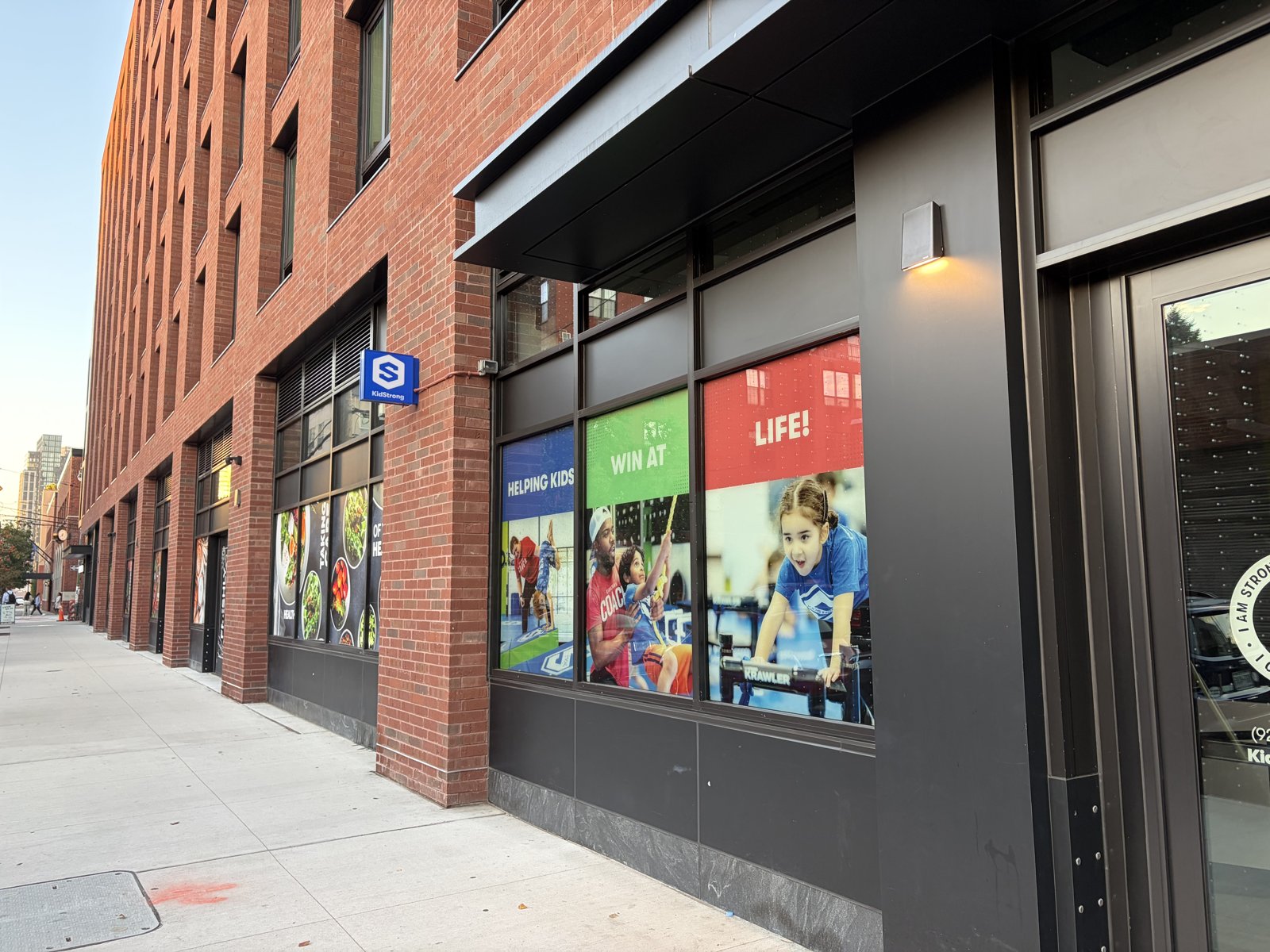 Red brick building with KidStrong window graphics showing kids climbing and the words Helping kids win at life