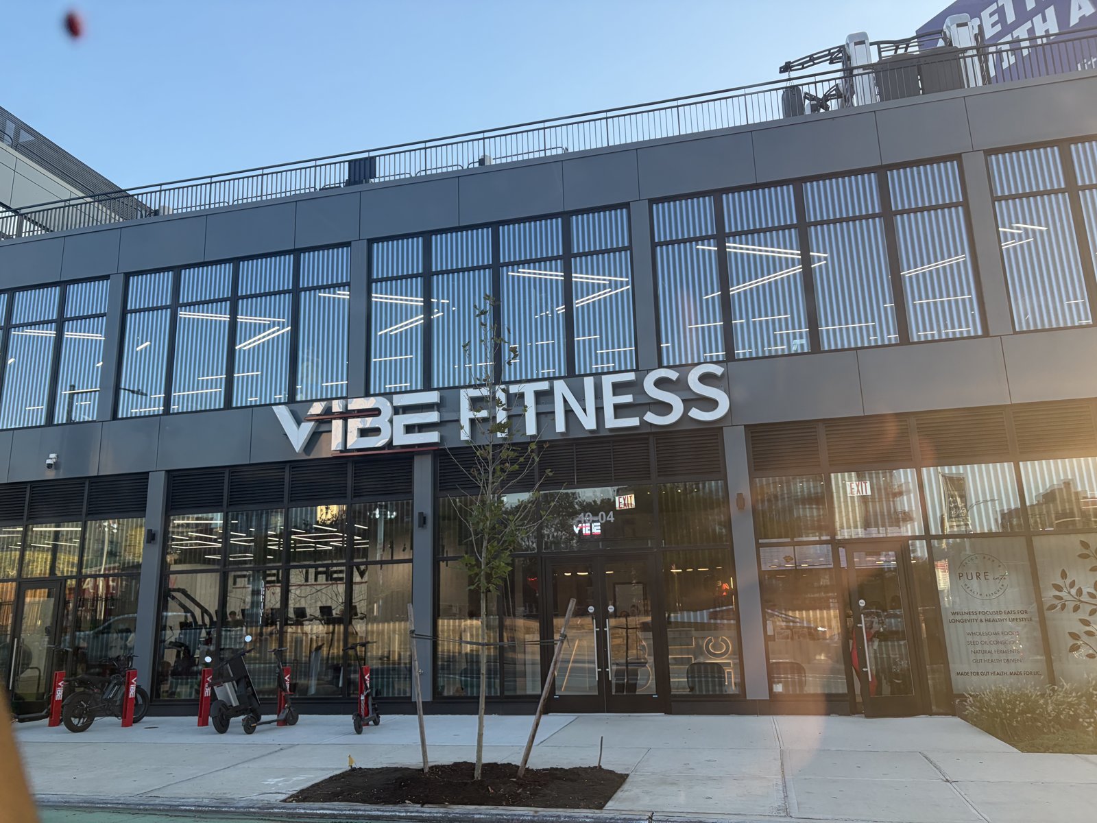 Two-story glass and dark panel building with large VIBE FITNESS letters above the entrance and bikes parked out front